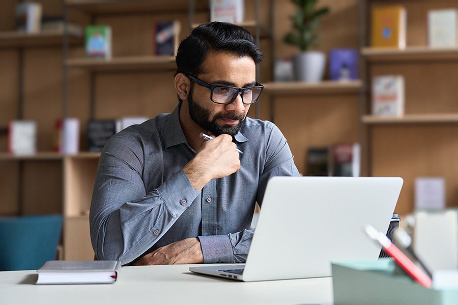 Claim Assistance - Portrait of a Young Businessman Sitting at His Desk in the Office While Using a Laptop