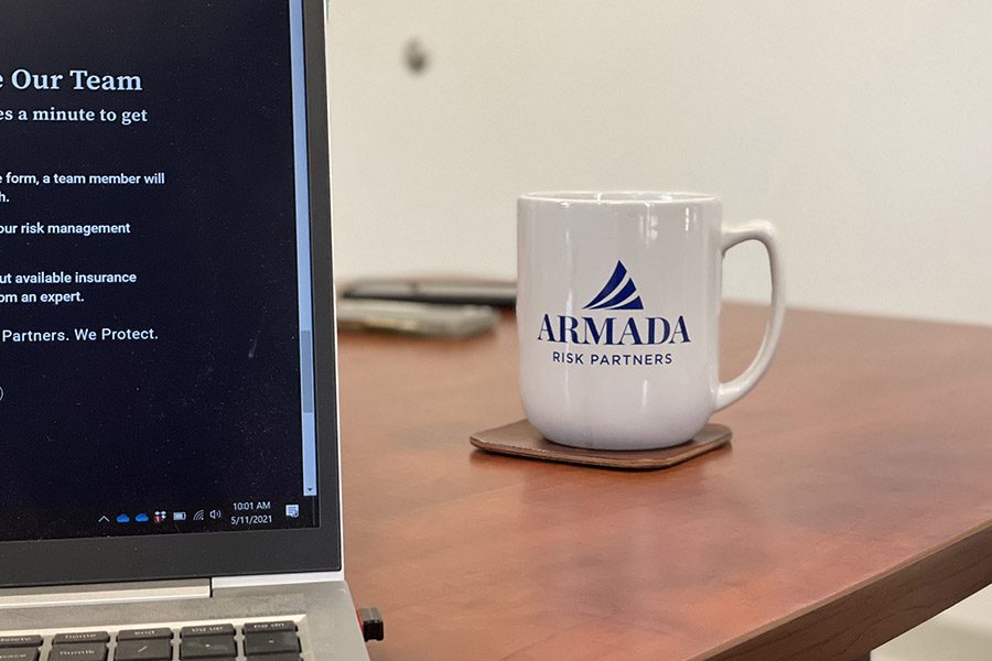 Join Our Fleet - Closeup View of a Laptop on a Wooden Table with an Armada Risk Partners Mug Next to it in the Office